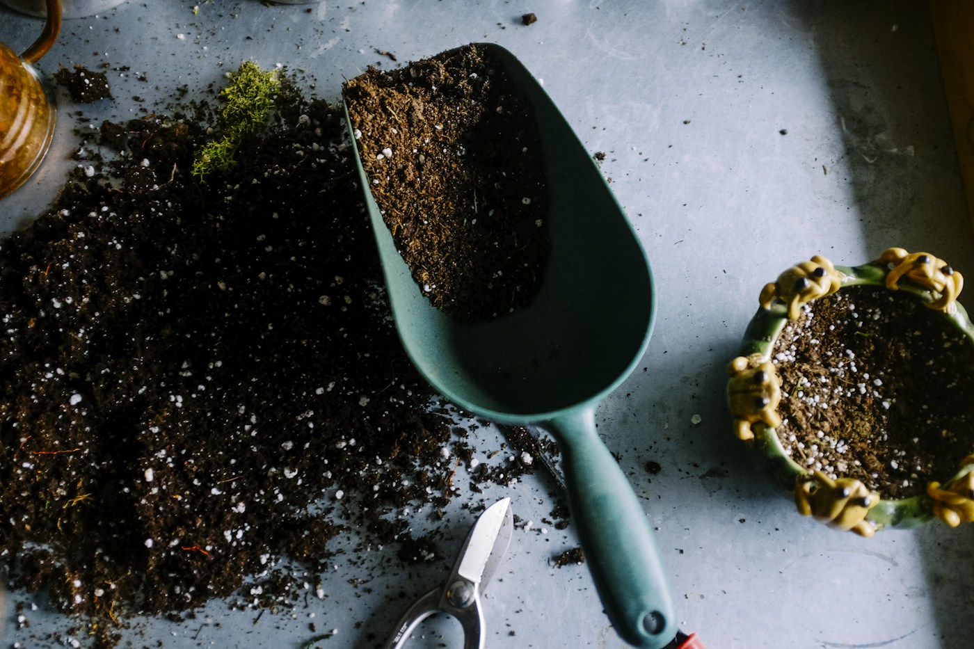 A green garden scoop, pruning scissors, and pots on a potting bench